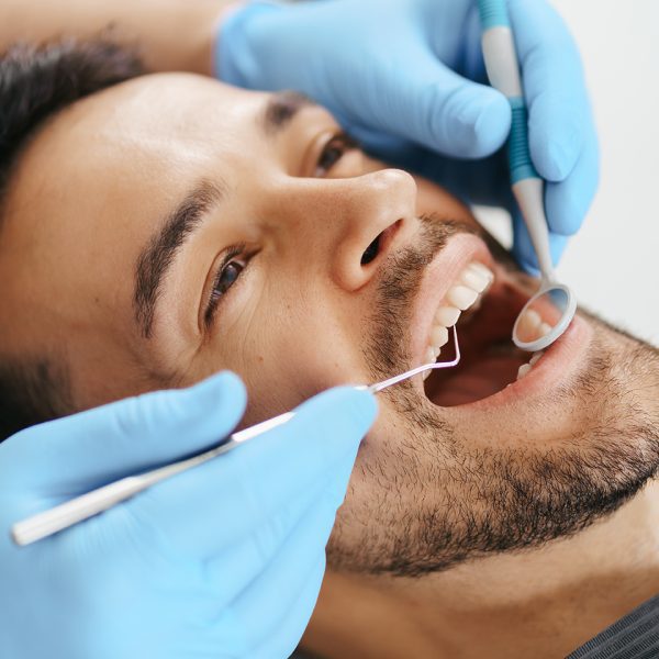 Smiling young man sitting in dentist chair while doctor examining his teeth